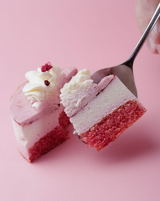 cheesecake manhattan con cuchara y dedos sobre fondo rosa para cheesecake avenue por dondykriga estudio madrid